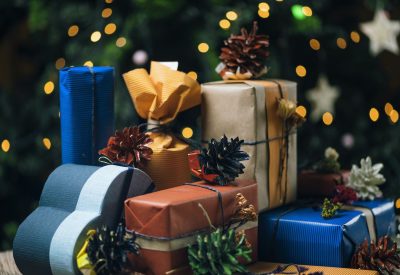 Christmas gifts in handmade boxes and decorated Christmas tree with colorful defocused lights in background.
